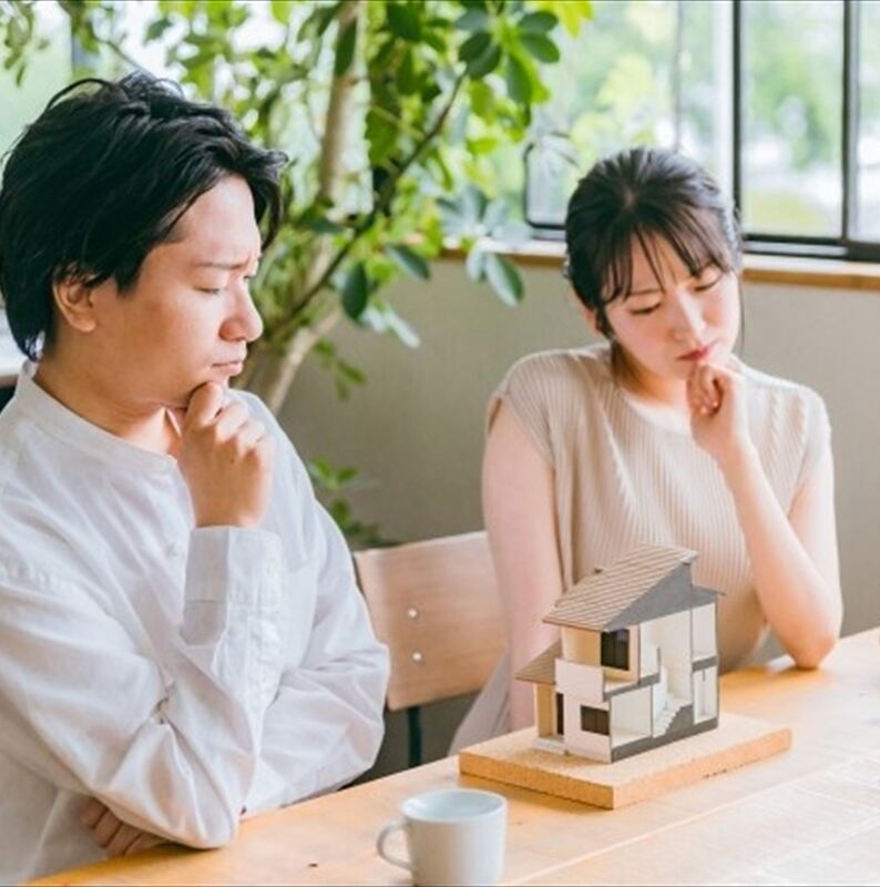 家の模型の前で考え込んでいる男女